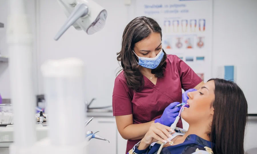 A dental Hygienist is cleaning the teeth of the patient