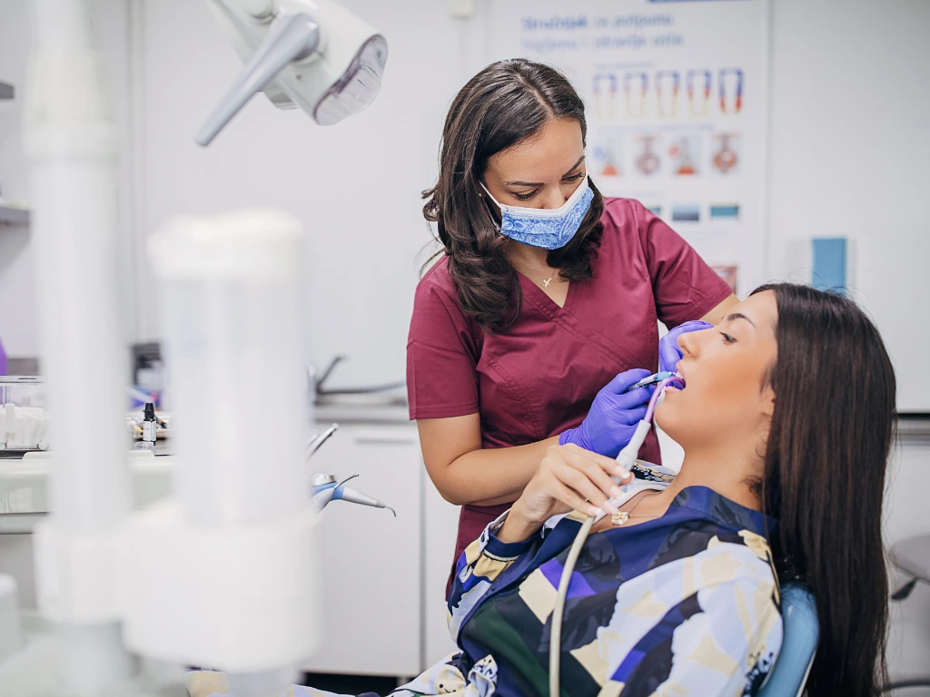 A dental Hygienist is cleaning the teeth of the patient