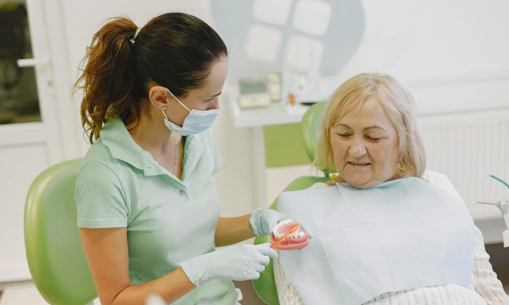 A dentist teaching an old woman on how to properly brush her teeth